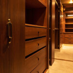 A Spacious Walk-In Closet With Custom Cabinets In A Houston Home Design, Featuring Warm Ambient Lighting And Rich Wood Textures.